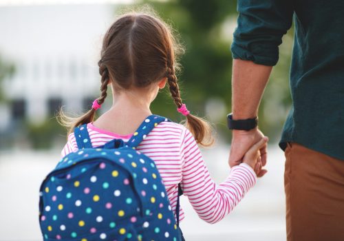 first day at school. father leads a little child school girl in first grade