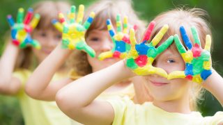 Happy child with painted hands against green spring background