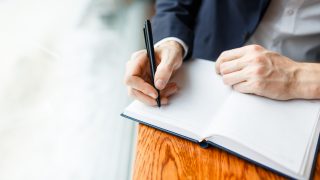 Human hands with pen writing down ideas on blank page of notebook