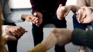 Close-up of people holding hands while attending group therapy.