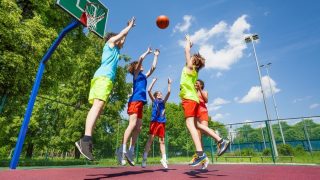 Children jump for flying ball during basketball game on the ground at sunny summer day together